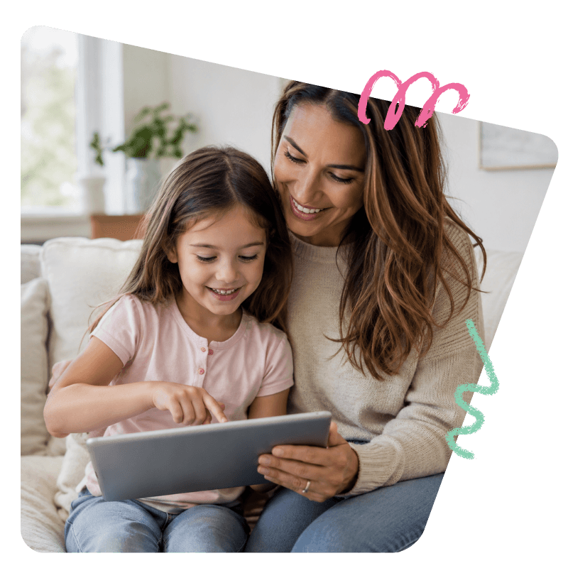 Una niña señalando la pantalla de una tablet mientras su mamá la acompaña en el sofá